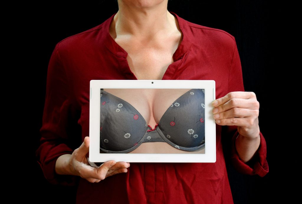 A picture of a woman wearing red and holding a picture of a woman's breast